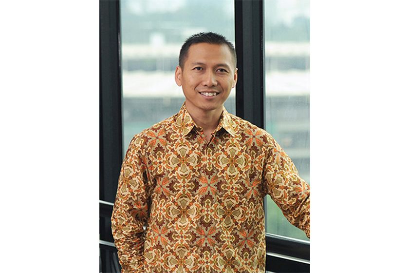 A man wearing batik shirt standing smiling near big window